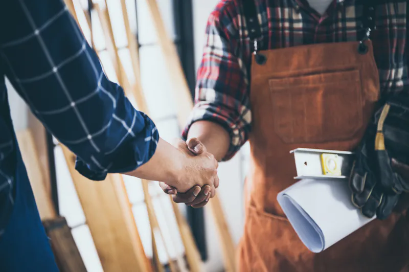 Ein Handwerker in Arbeitsschürze und ein Kunde schütteln sich die Hände zur erfolgreichen Partnerschaft bei Disselnmeyer Holz.