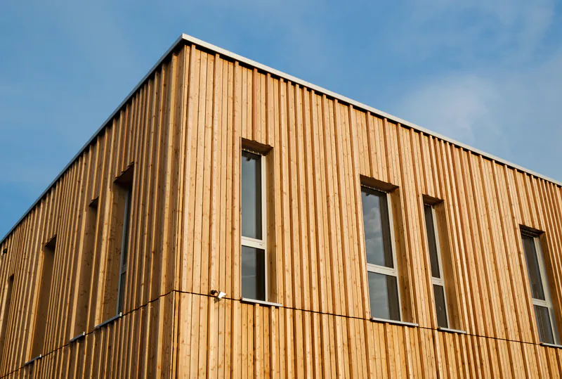 holzfassade-holz-disselnmeyer-205eb217 Moderne vertikale Holzfassade von Holz Disselnmeyer an einem Gebäude mit schmalen Fenstern vor blauem Himmel.